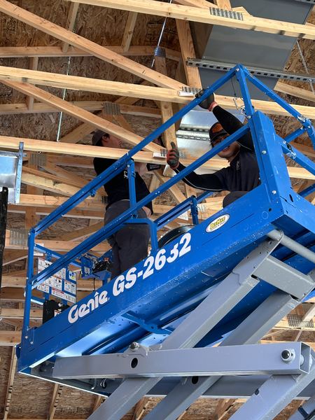 Two Five Star techs hanging commercial ductwork from a Genie scissor lift