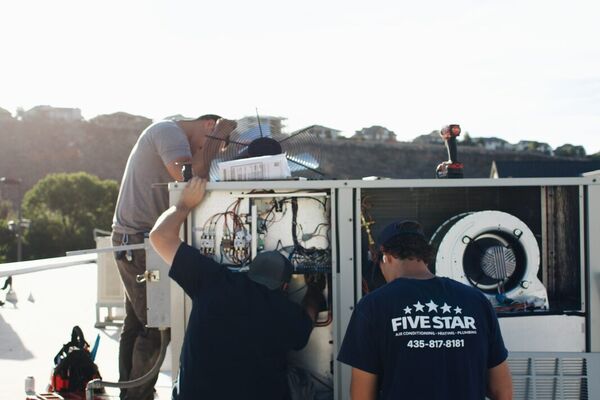 Three Five Star technicians servicing a commercial rooftop package unit at sunset in St. George, Utah